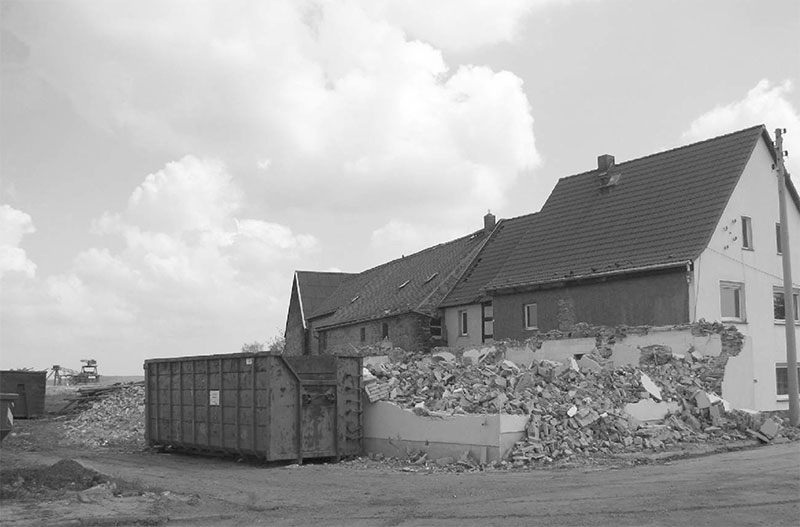Heuersdorf, Abbruch der ersten Häuser. Im Hintergrund ist der Abraumbagger aus dem Tagebau zu sehen.
